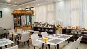 A hotel dining area with tables and chairs, buffet setup, and a decorative thatched structure. - Dao Ngoc Hotel (Da Nang)
