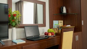 A hotel room with a wooden desk, a laptop, a vase with flowers, a plate of fruit, a coffee maker, and a mirror. - Dao Ngoc Hotel (Da Nang)