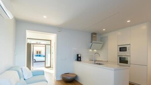 Um espaço de estar moderno e compacto, com cozinha americana, sofá e pequena área de refeições.