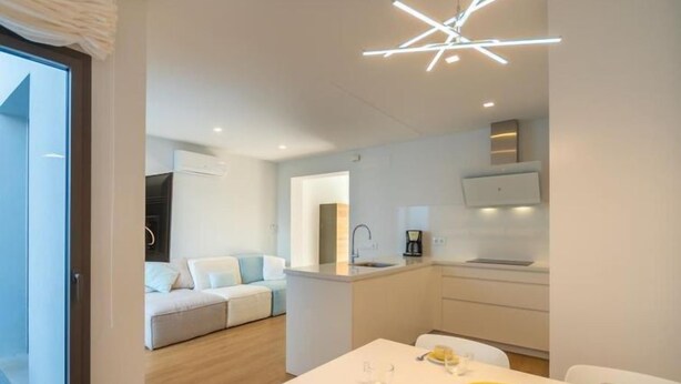 Quarto moderno e bem iluminado, com uma mesa de jantar posta para dois, uma cozinha compacta e uma sala de estar com sofá.