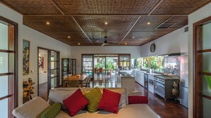 A spacious living area with a wooden ceiling, a sofa with cushions, a dining area, and a kitchen with modern appliances. - Villa Claudia  (Kerobokan)