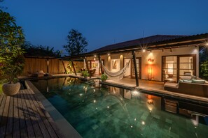 Un área de piscina moderna con una hamaca, asientos exteriores y un patio bien iluminado.