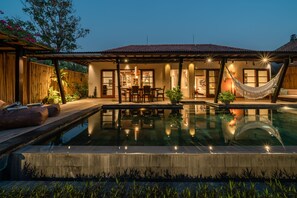 Un área de piscina con una mesa de comedor y sillas, una hamaca y una zona de estar cubierta.