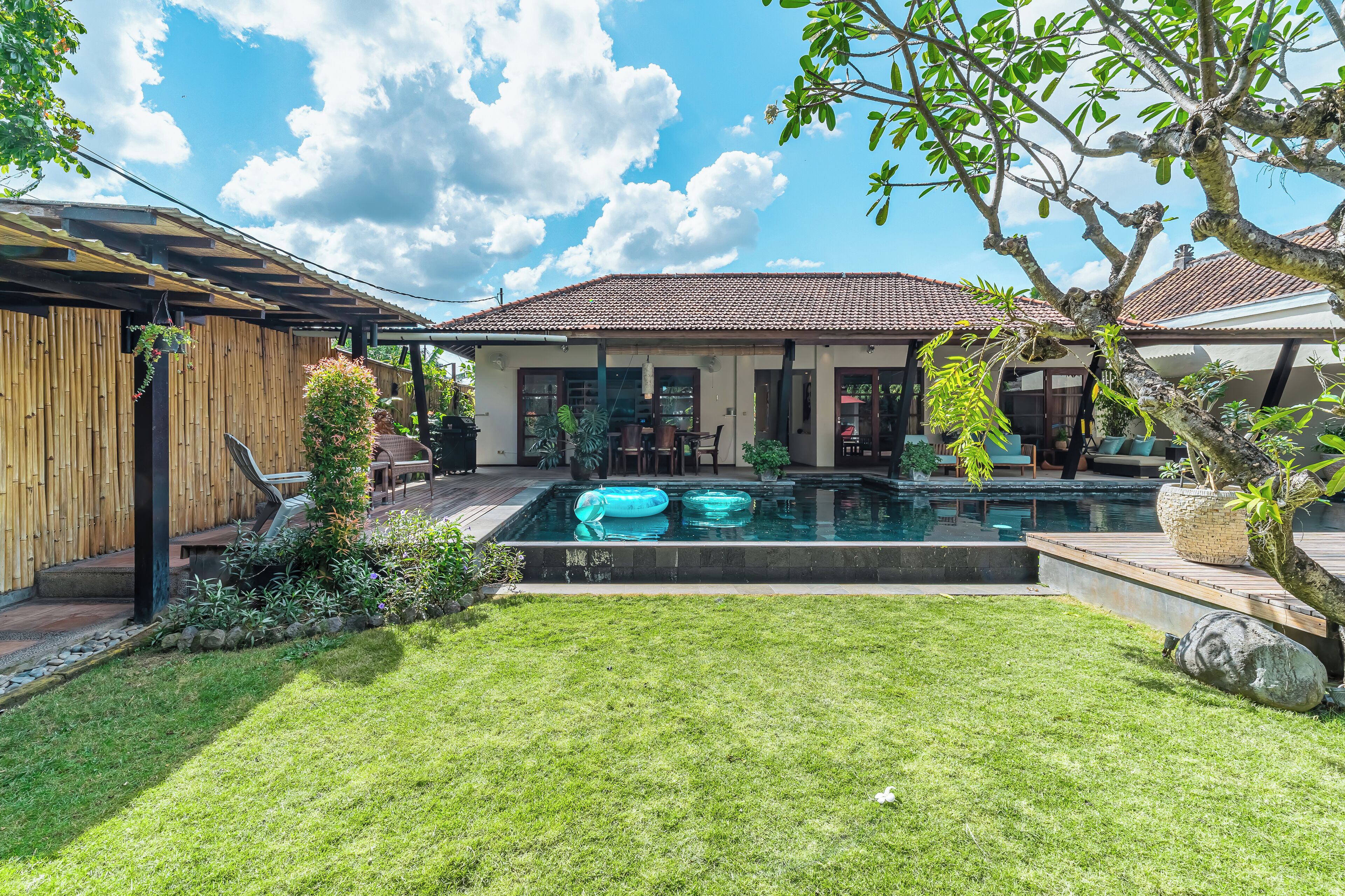 Ein Garten mit Swimmingpool, einer Holzterrasse und einem Bambuszaun.