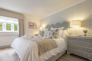 A neatly made bed with white linens and a beige throw blanket, a bedside lamp, and a dresser with drawers. - The Beach House (B), Brancaster, Norfolk (Brancaster)