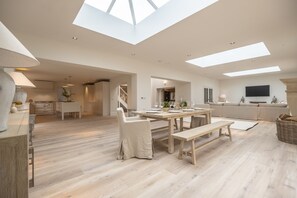 A spacious living area with a high ceiling and skylights, a dining area with wooden furniture, and a cozy seating area with a sofa and TV. - The Beach House (B), Brancaster, Norfolk (Brancaster)