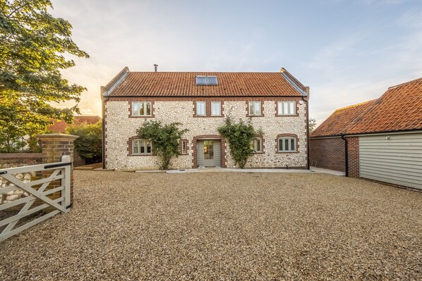 A two-story stone building with a tiled roof, a gravel driveway, and a wooden gate. - The Beach House (B), Brancaster, Norfolk (Brancaster)
