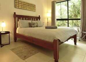 A neatly made bed with a wooden frame, a bedside lamp, and a view of greenery through a window. - Misty Mountains Rainforest Retreat  (Bellenden Ker)