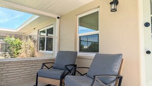 A covered porch with two wicker rocking chairs, a striped rug, and a door with a light fixture. - Peaceful Beach Home Fully Equipped! (Sarasota)