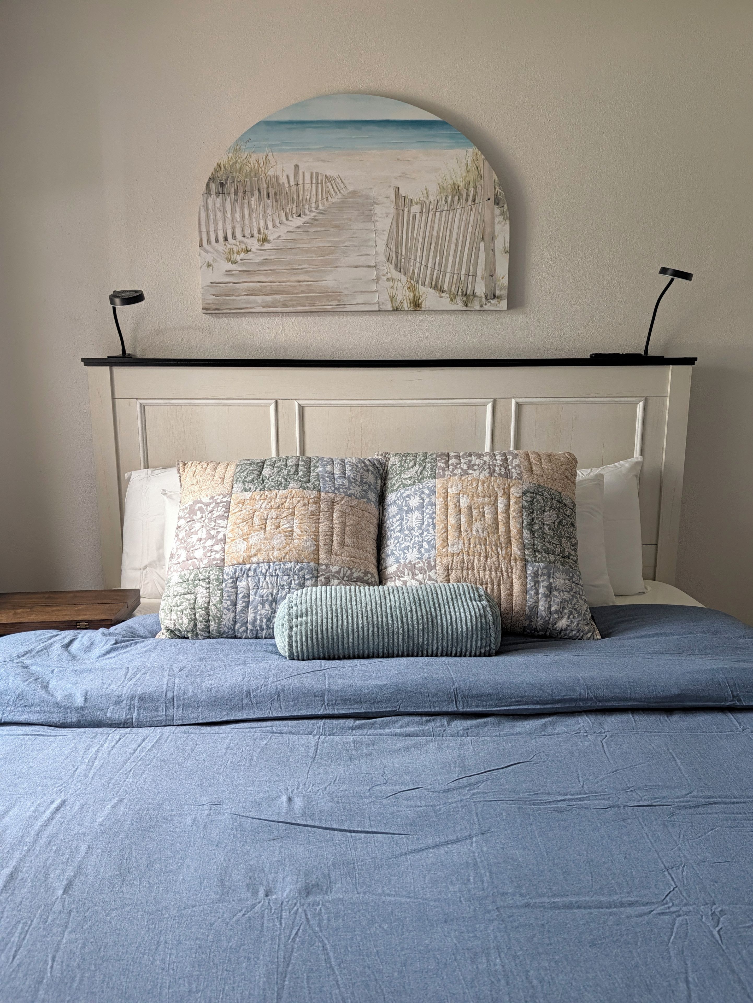 Une chambre à coucher avec un lit, une tête de lit, un tableau accroché au mur et deux lampes de chevet.