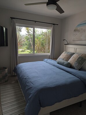 A bedroom with a bed, a ceiling fan, a window with curtains, and a wall-mounted artwork.