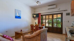 Un salon avec un canapé, une petite table et un téléviseur. On y trouve également un coin repas avec des chaises et une table. Une grande fenêtre offre une vue sur la verdure.