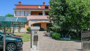 Une maison à deux étages, avec une arche en pierre menant à l’entrée, une allée pavée et une voiture garée.