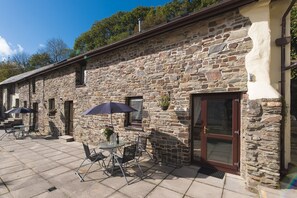 A stone building with a patio area featuring outdoor seating and umbrellas. - Royd Cottage at Lower Aylescott (West Down)
