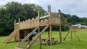 Une structure de jeux en bois comprenant un toboggan, des balançoires et une table de pique-nique.
