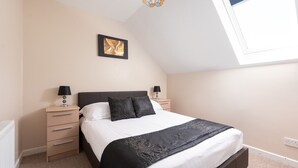 A bedroom with a bed, bedside tables, lamps, a framed picture, and a skylight.