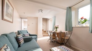 A living room with a sofa, ottoman, dining table, chairs, and a staircase leading to another room. - Smithy Cottage at Lower Aylescott (West Down)