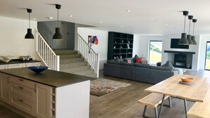 Et moderne køkken med en central ø, et spiseområde med et træbord, en grå sofa og en trappe til en repos.