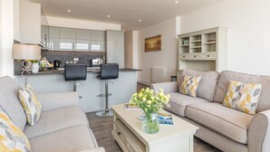 A modern living room with a sofa, two chairs, a coffee table with a vase of flowers, and a kitchen area with a counter and cabinets. - 8 Hartland, sleeps 6 with sea view (Esplande, Woolacombe)