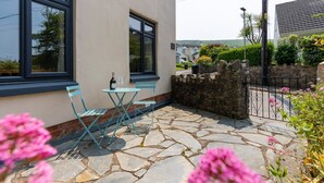 A stone patio with a table and chairs, a bottle of wine, and a view of the sea.