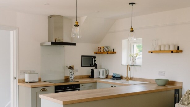 A modern kitchen with a central island, wooden countertops, and pendant lighting.