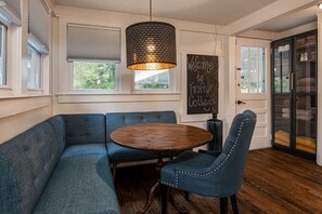 Ein gemütliches Zimmer mit einem blauen Ecksofa, einem runden Holztisch und einem dunkelblauen Stuhl. An der Tafel steht: Willkommen im Firefly Cottage.