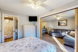 Un dormitorio con cama, cómoda, ventilador de techo, televisor y un sofá en la sala de estar contigua.