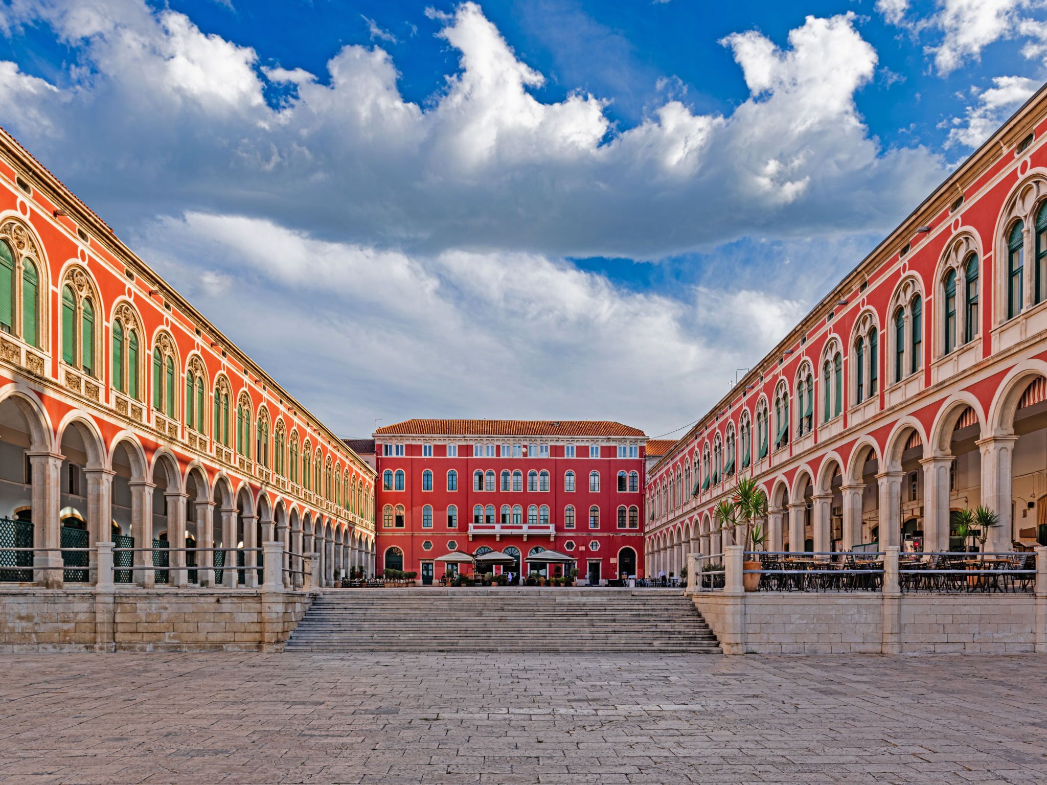 A red building with arched windows and a central courtyard with steps leading to a covered area.