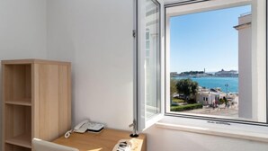 A room with a wooden desk, a chair, a telephone, and a window with a view of a body of water and buildings. - Lara's House by Interhome (Split)