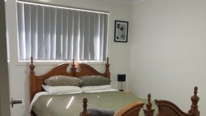 A bedroom with a wooden bed, a window with blinds, a framed picture on the wall, and a door. - Stylish Retreat in Macquarie Links - Golf, Comfort & Tranquility (Macquarie Links)