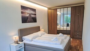 A modern bedroom with a large bed, bedside lamps, a wooden wardrobe, and a view of the outdoors. - Seezugang & Ski Ossiacher See by Interhome (Bodensdorf)