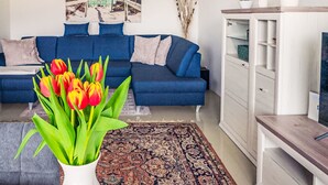 A living room with a blue sofa, a patterned rug, a white vase with tulips, and a painting of a beach scene. - Seezugang & Ski Ossiacher See by Interhome (Bodensdorf)
