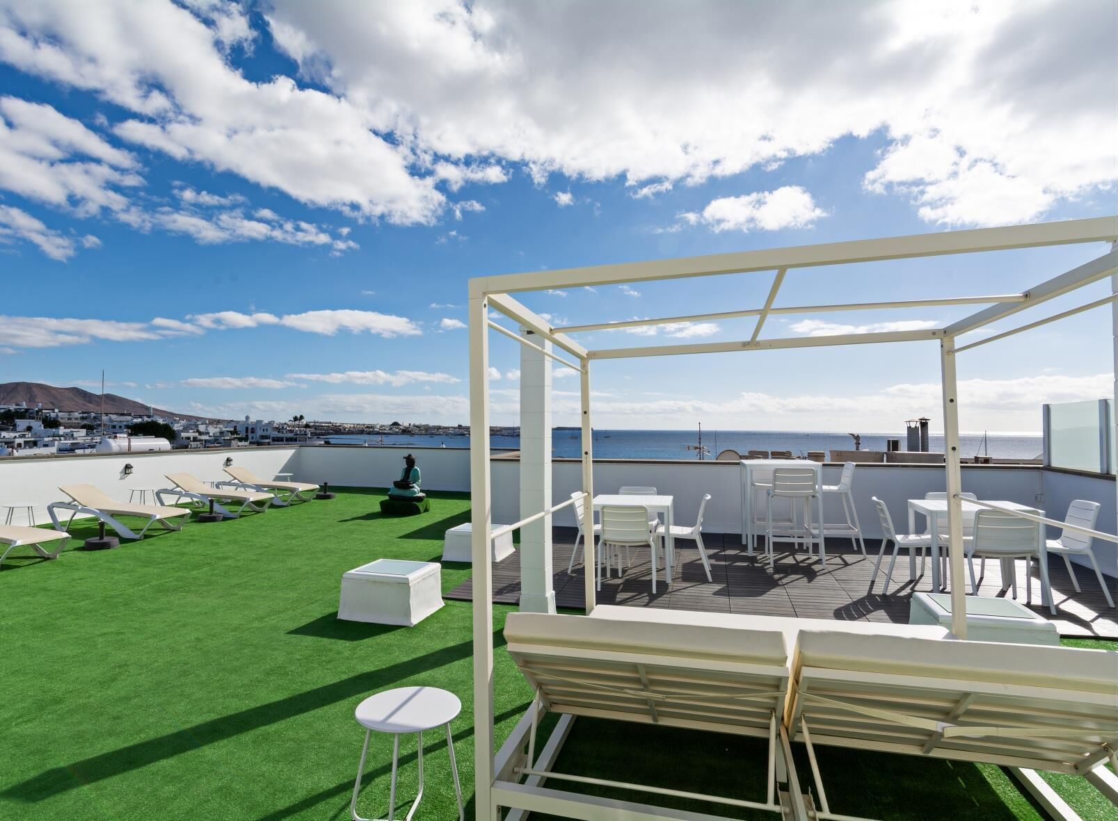 A rooftop terrace with a clear view of the sea, furnished with white chairs and tables, and a green lawn area.