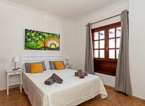 Une chambre à coucher bien rangée, avec un lit, deux tables de chevet, un tableau et une fenêtre avec des rideaux.