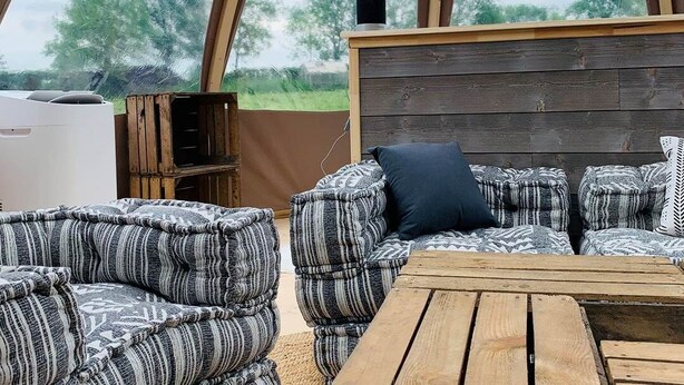 A cozy outdoor seating area with a wooden table and cushioned sofas under a large, curved wooden structure. - Starry Wigwam (pets not allowed) (MESSEY SUR GROSNE)