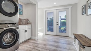 A laundry room with a washing machine and dryer, a small cabinet, and a door leading to a patio area. - 1449 Braman Ave (Fort Myers)