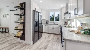 A modern kitchen with white cabinets, a built-in refrigerator, a window, and a countertop with kitchen essentials. - 1449 Braman Ave (Fort Myers)