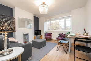 Relax in a stylish living space with a sofa, ottoman, and dining area, featuring a large window and chandelier.