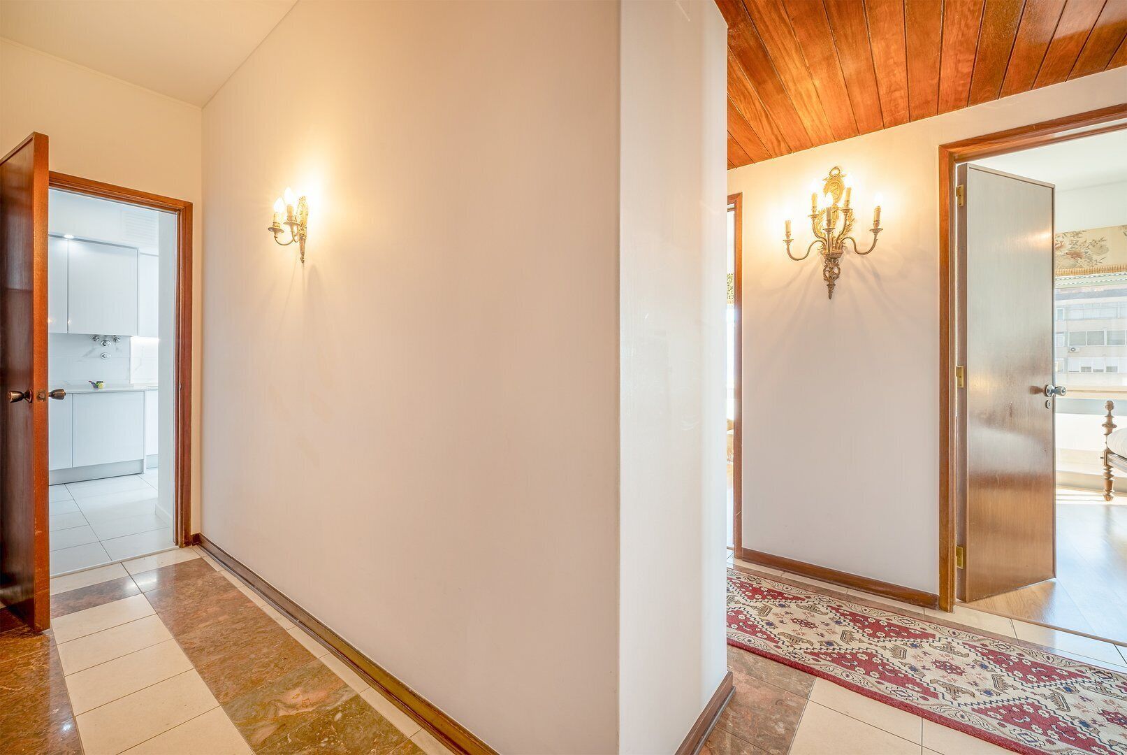 Un corridoio con soffitto in legno e un tappeto a motivi geometrici che conduce a una stanza con un letto.