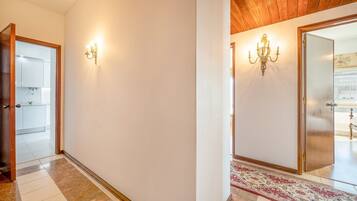 Un corridoio con soffitto in legno e un tappeto a motivi geometrici che conduce a una stanza con un letto.