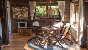 Une pièce chaleureuse avec un décor intérieur en bois, une table ronde entourée de chaises, un téléviseur et une fenêtre avec des rideaux.