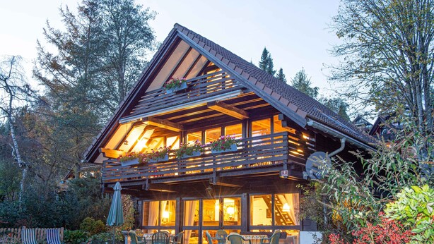 Un chalet en bois doté d’un balcon, d’un espace salon extérieur et d’un jardin.