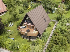 A wooden cabin with a deck, surrounded by lush greenery.