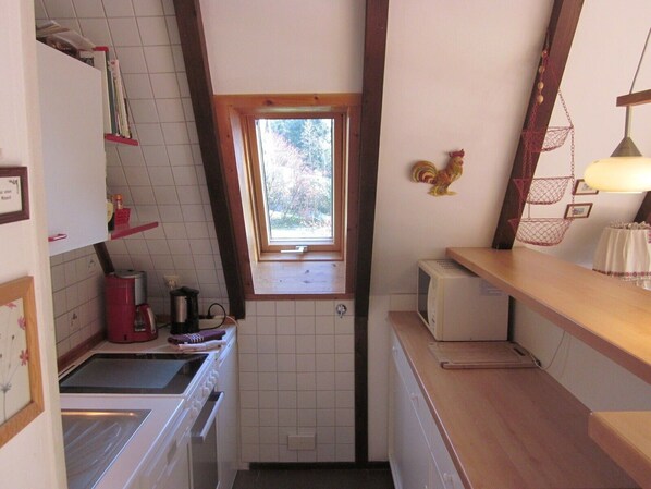 Een kleine keuken met een raam, een magnetron en een spoelbak.