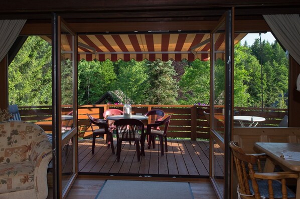 An outdoor deck with a wooden table and chairs, surrounded by a wooden railing, and a covered area with a striped awning.