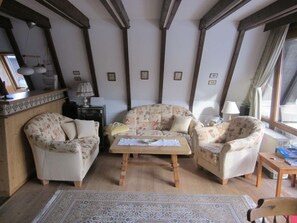 A cozy living room with wooden beams, floral-patterned furniture, a central coffee table, and a patterned rug.