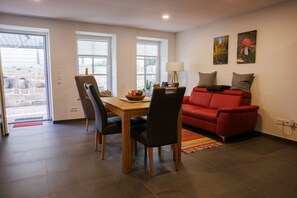 A dining area with a table, chairs, a red sofa, and two paintings on the wall. - Apartment 'Alter Kuhstall' with Private Terrace and Wi-Fi (Neuenstein)
