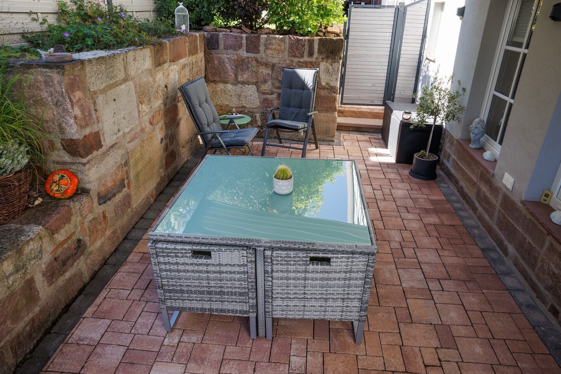 Un patio con una mesa de vidrio, sillas de mimbre y una planta en maceta.