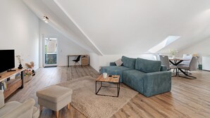 Un loft moderno con techos altos, una zona de estar acogedora con sofá y reposapiés, una mesa de comedor con sillas y un televisor sobre un mueble de madera.