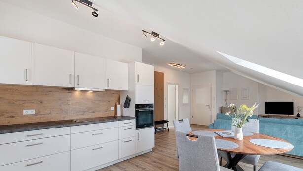 Una cocina moderna con armarios blancos, encimera de madera y comedor con sillas grises y una mesa de madera.